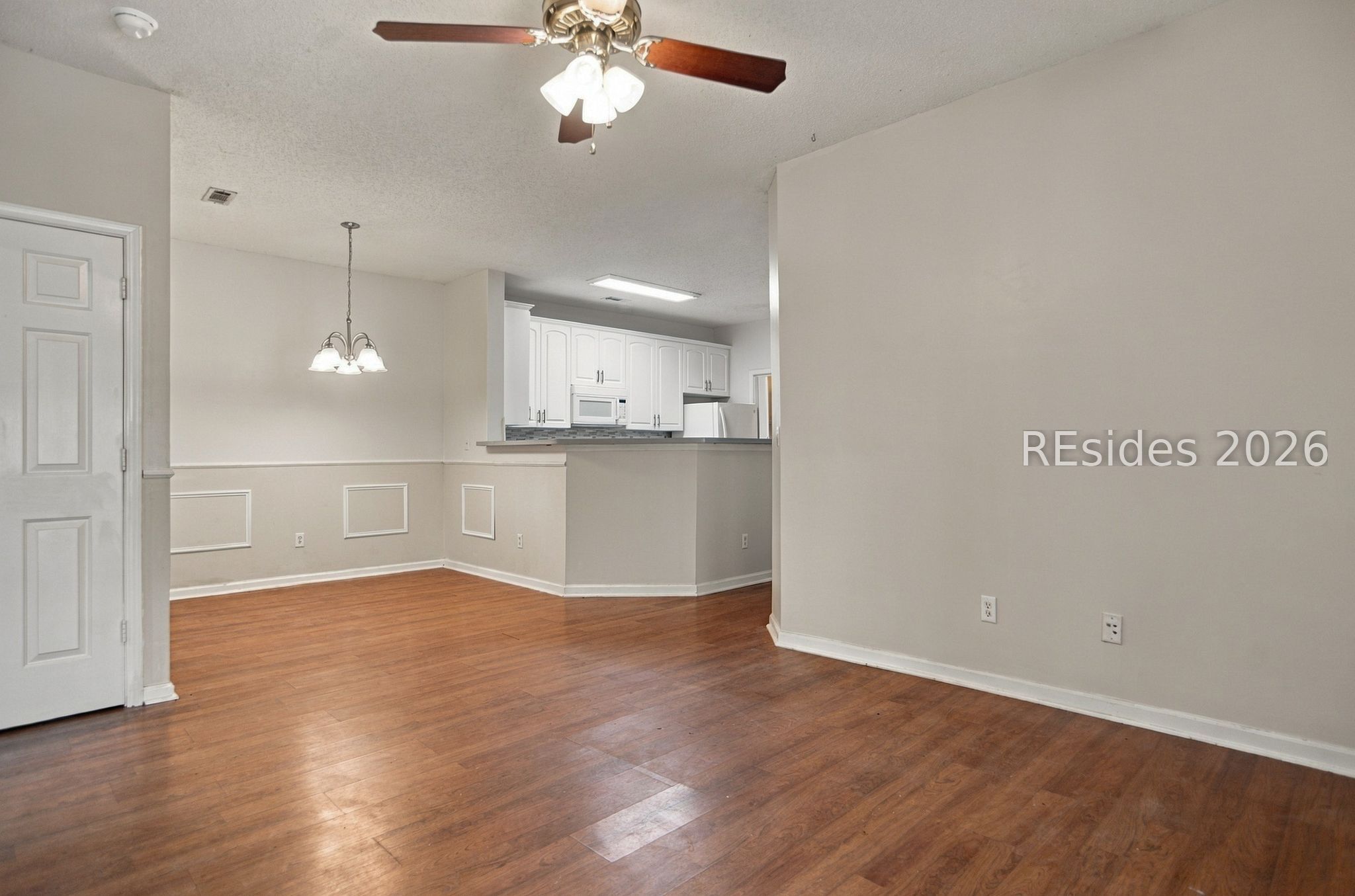 Vacant dining area with wood floors, decorative wall paneling, and an open kitchen.