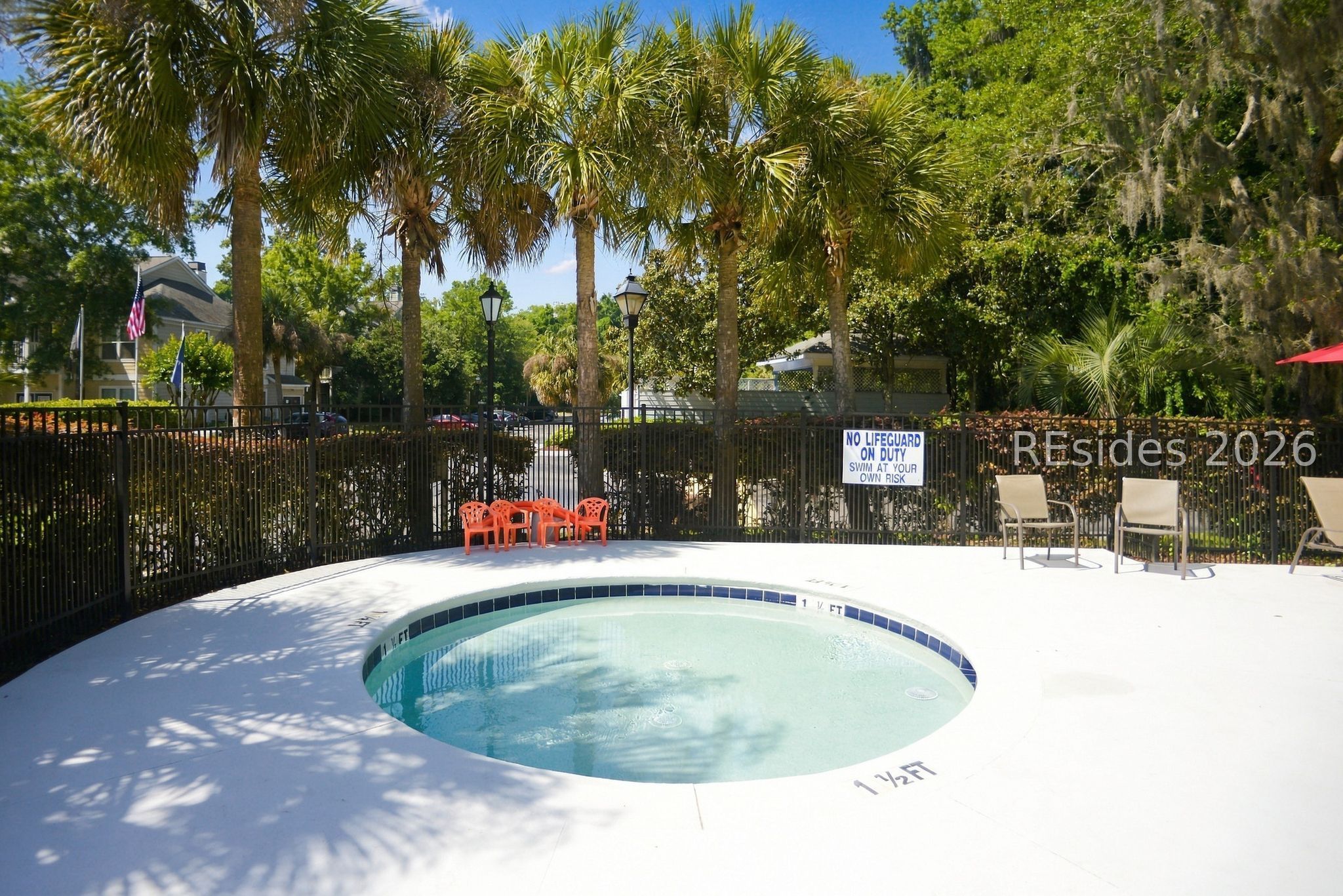 Shallow circular community pool with palm trees, deck chairs, and a no-lifeguard sign.