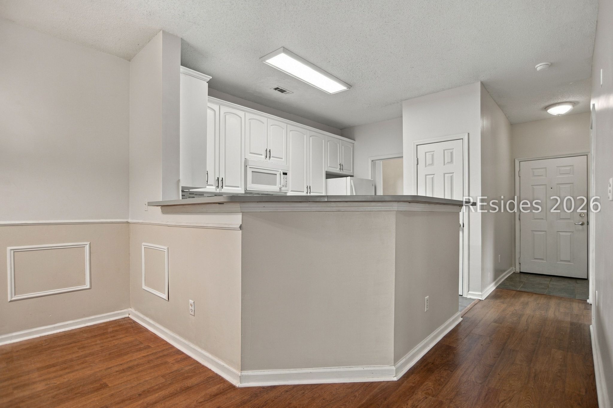 Unfurnished kitchen with white cabinets and a breakfast bar opening onto the entry hall.