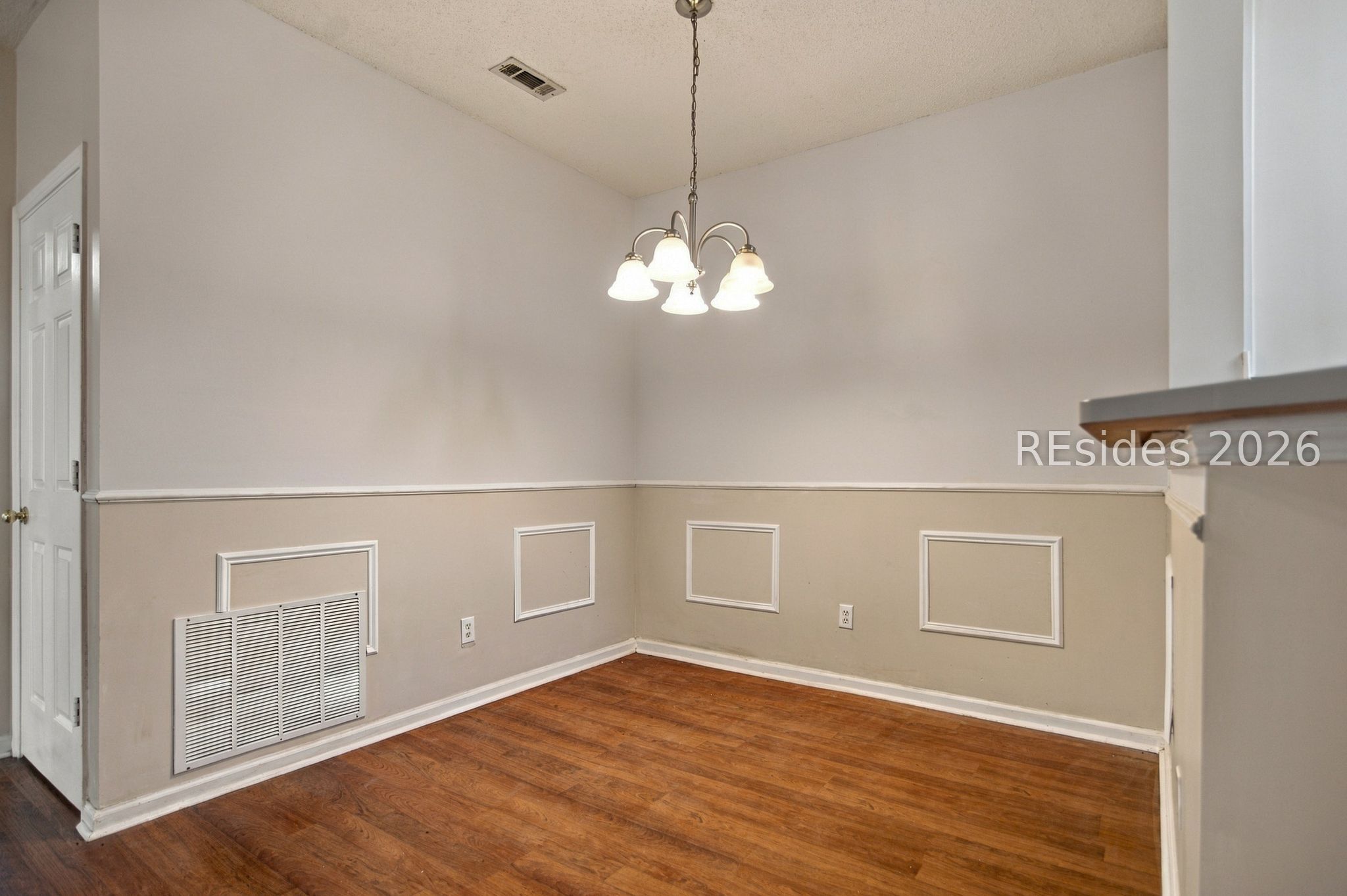 Empty dining area with hardwood floors, decorative wall molding, and a five-light chandelier.