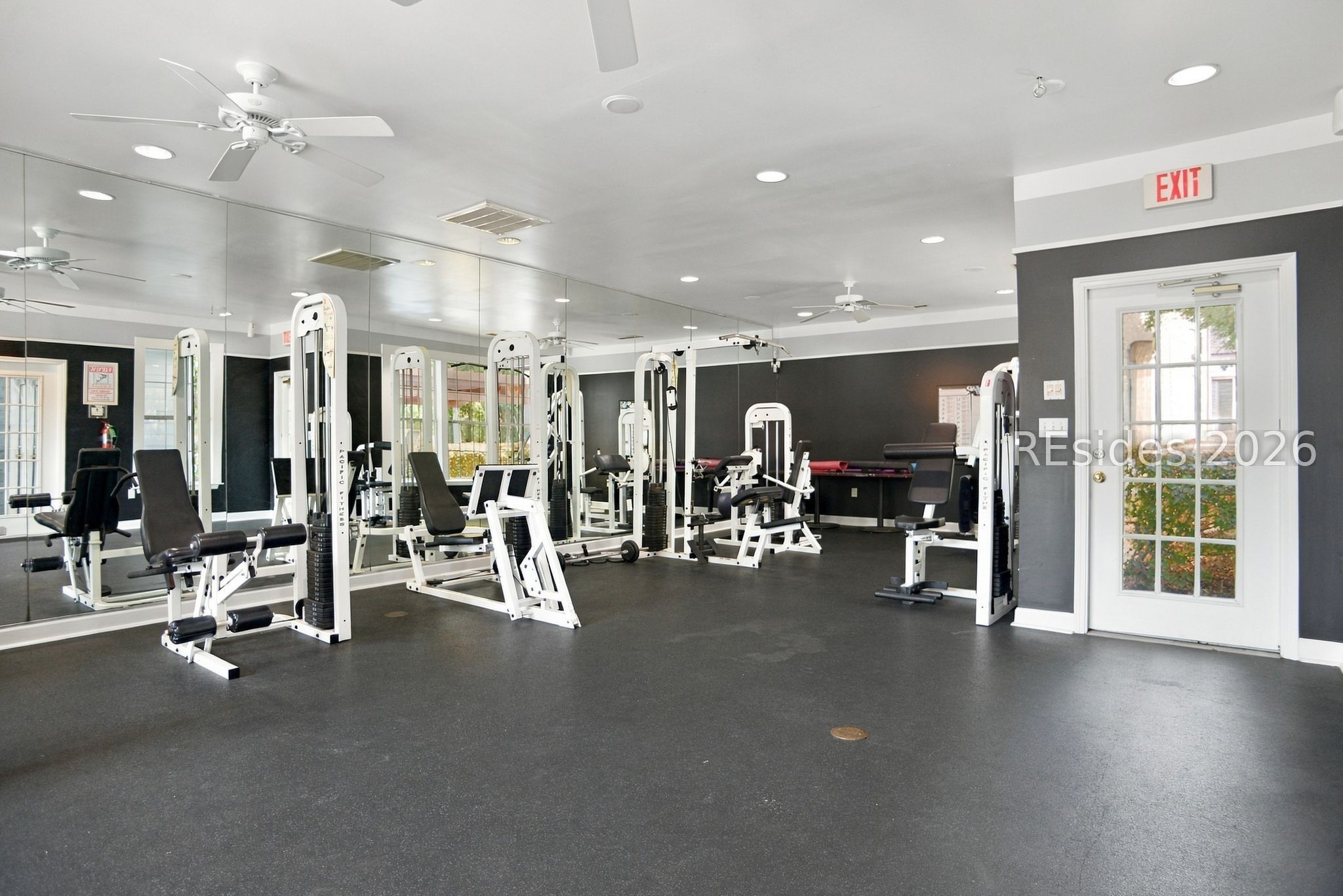 Fitness room with white weight machines, mirrored walls, and black rubber flooring.