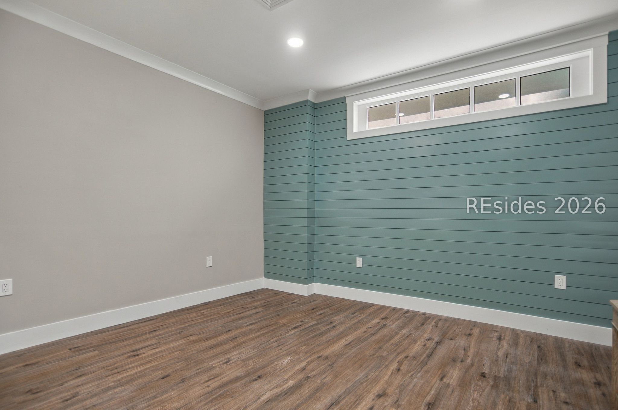 Empty room with a teal paneled accent wall, high clerestory windows, and wood-look flooring.