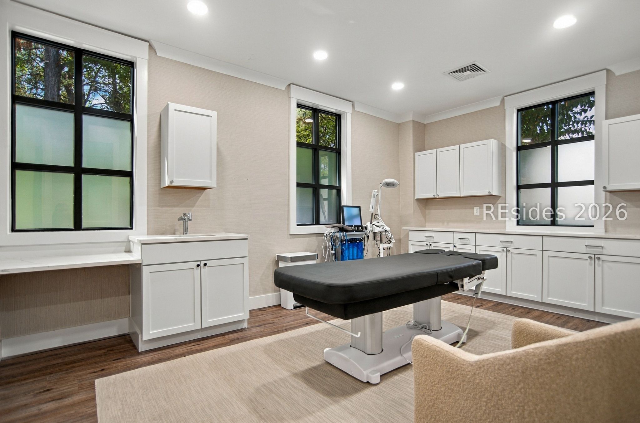 Medical treatment room with a black examination table, diagnostic equipment, and large windows.