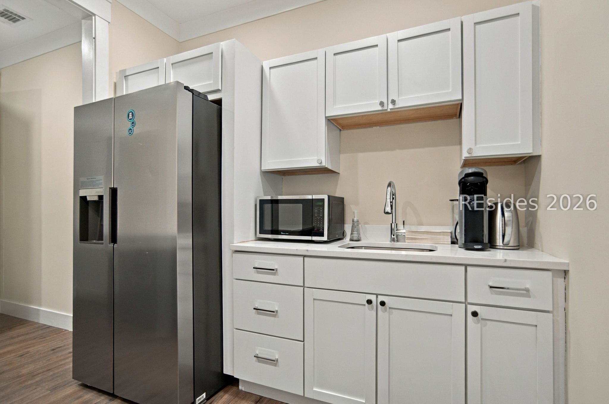 Kitchen with white cabinetry, stainless steel refrigerator, microwave, and sink.
