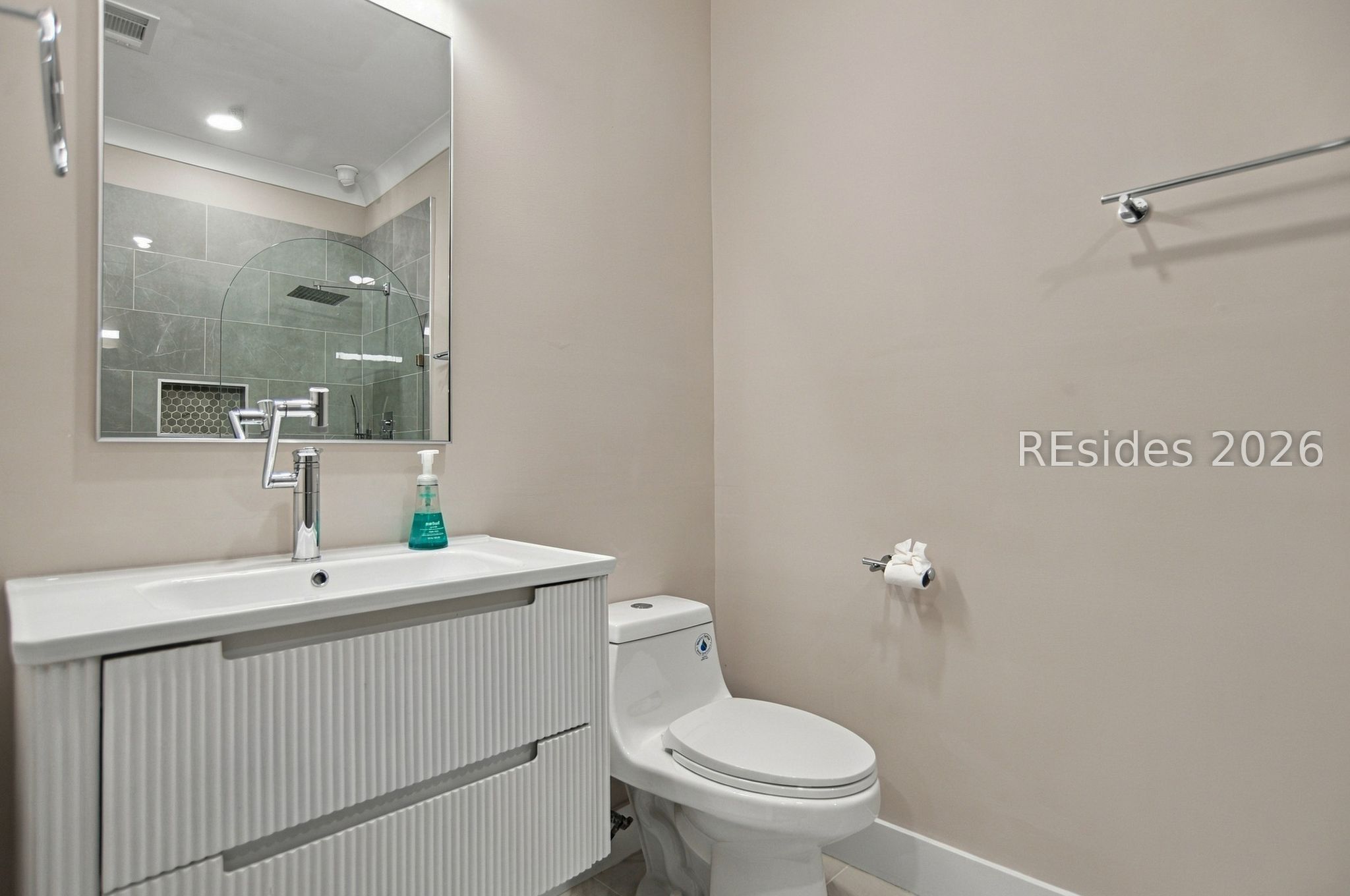 Bathroom with a fluted white vanity and toilet; the mirror reflects a gray-tiled walk-in shower.