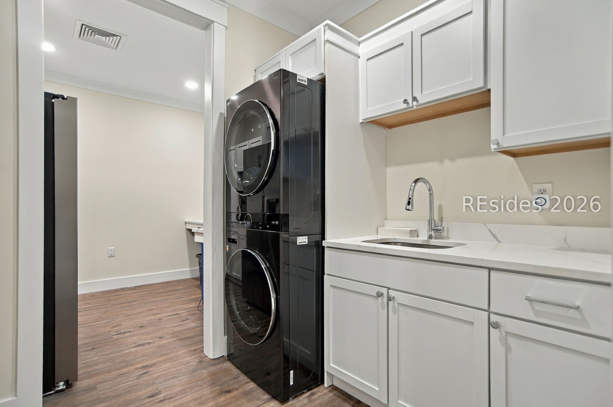 Laundry room with stacked black washer and dryer, white cabinetry, and a sink.