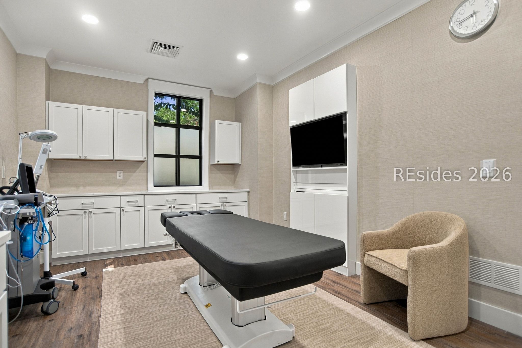 Medical examination room with an adjustable exam table, built-in cabinets, and medical equipment.