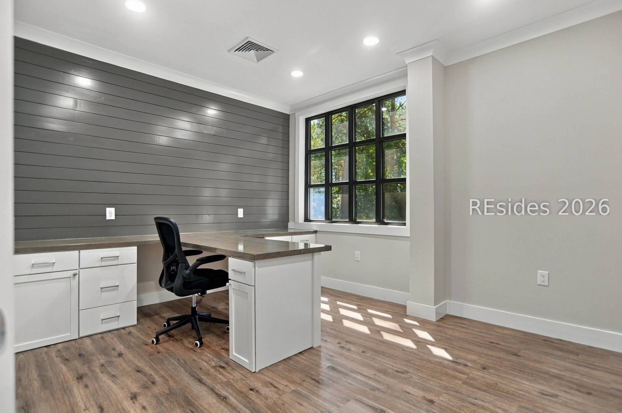 Office with a built-in desk, gray plank accent wall, and large black-framed window.