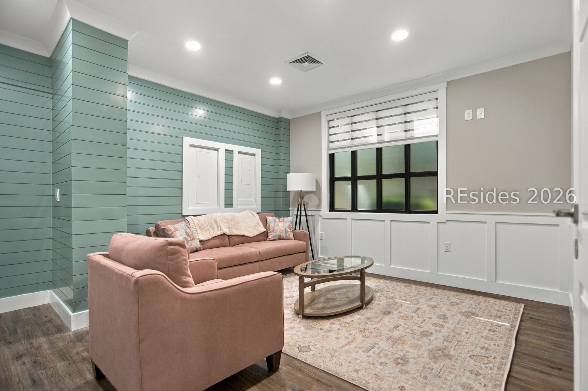Living room with blush sofas, teal paneled wall, black-grid window, and glass coffee table.