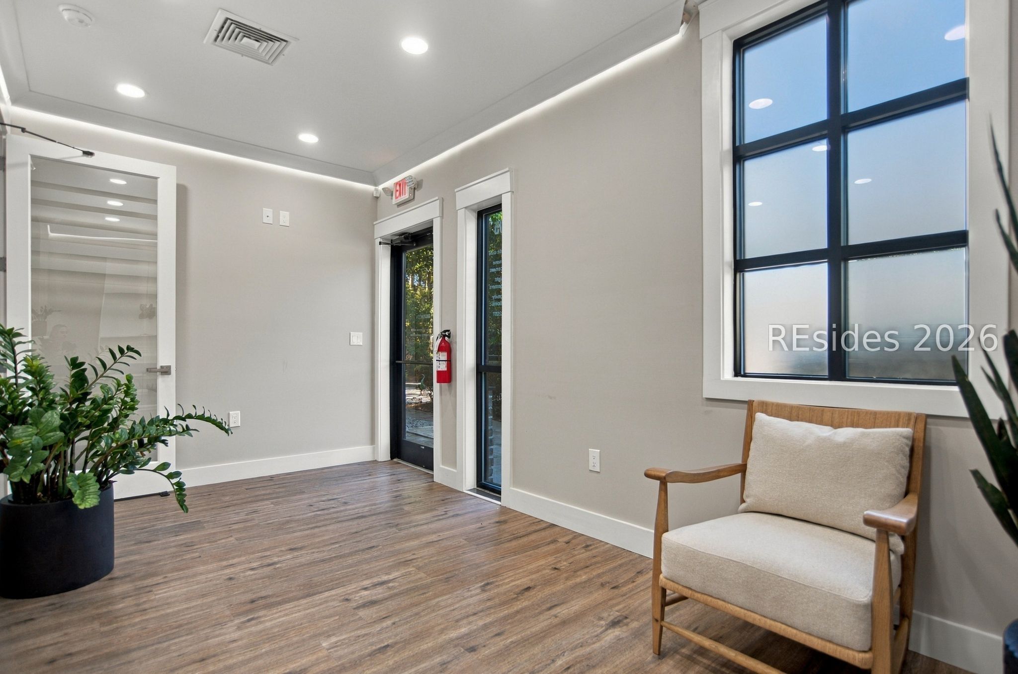 Furnished entry area with black-framed windows, a wooden armchair, and a potted plant.