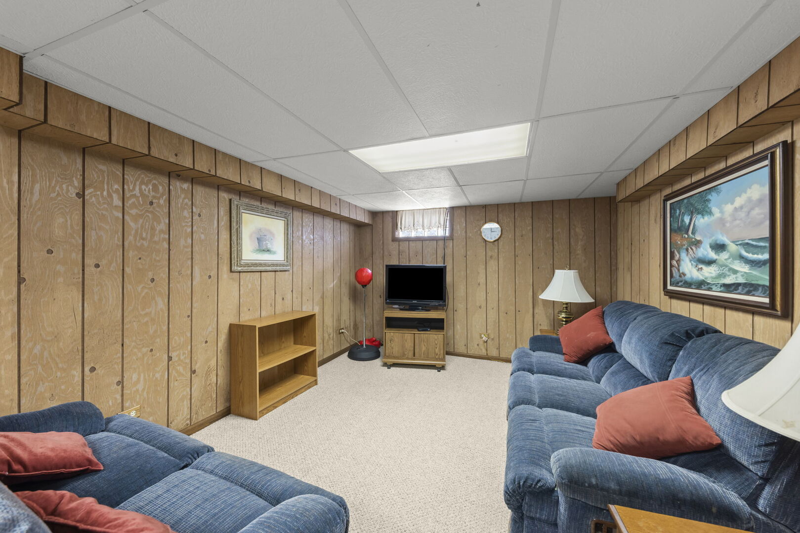 Basement family room with wood-paneled walls, blue sofas, and a television.