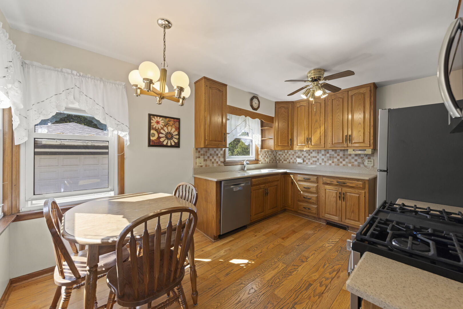 Kitchen with oak cabinetry, hardwood floors, and a dining table beside a large window.