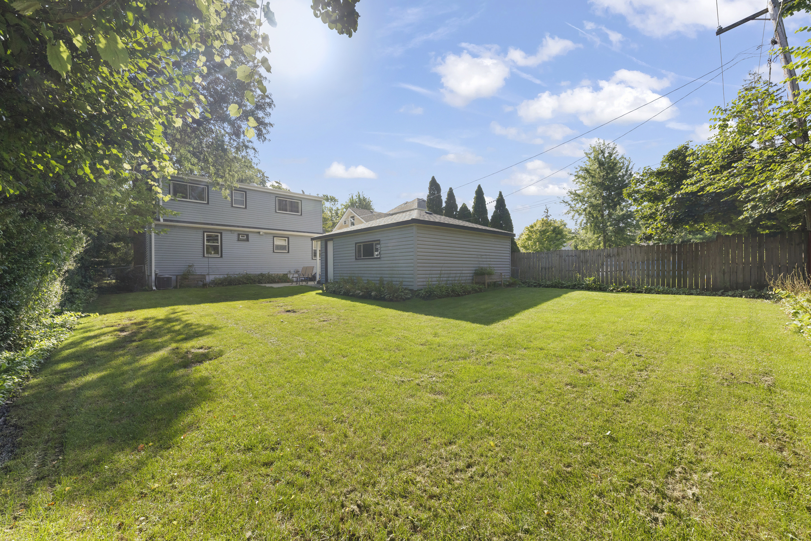 Gray two-story house and detached garage behind a broad, fenced lawn.