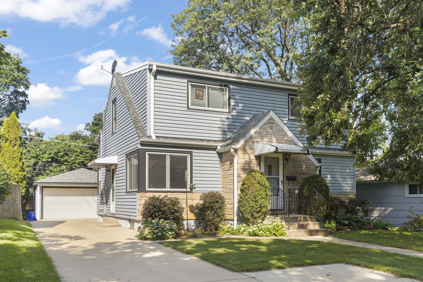 Two-story gray-sided home with a stone entry, attached garage, and landscaped front yard.