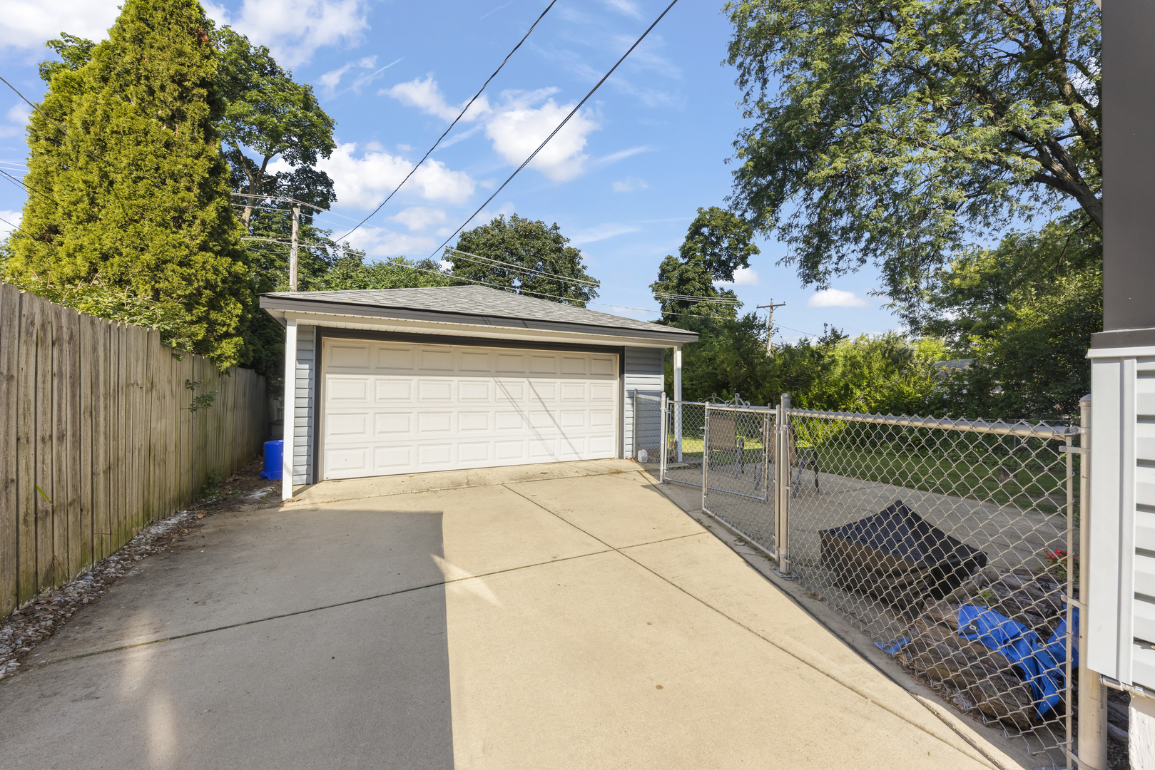 Detached garage at the end of a concrete driveway, with a chain-link gate and wooden fence.