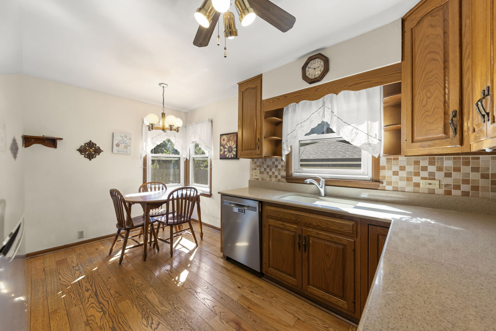Kitchen with oak cabinets, tiled backsplash, and a small dining table beside sunny windows.