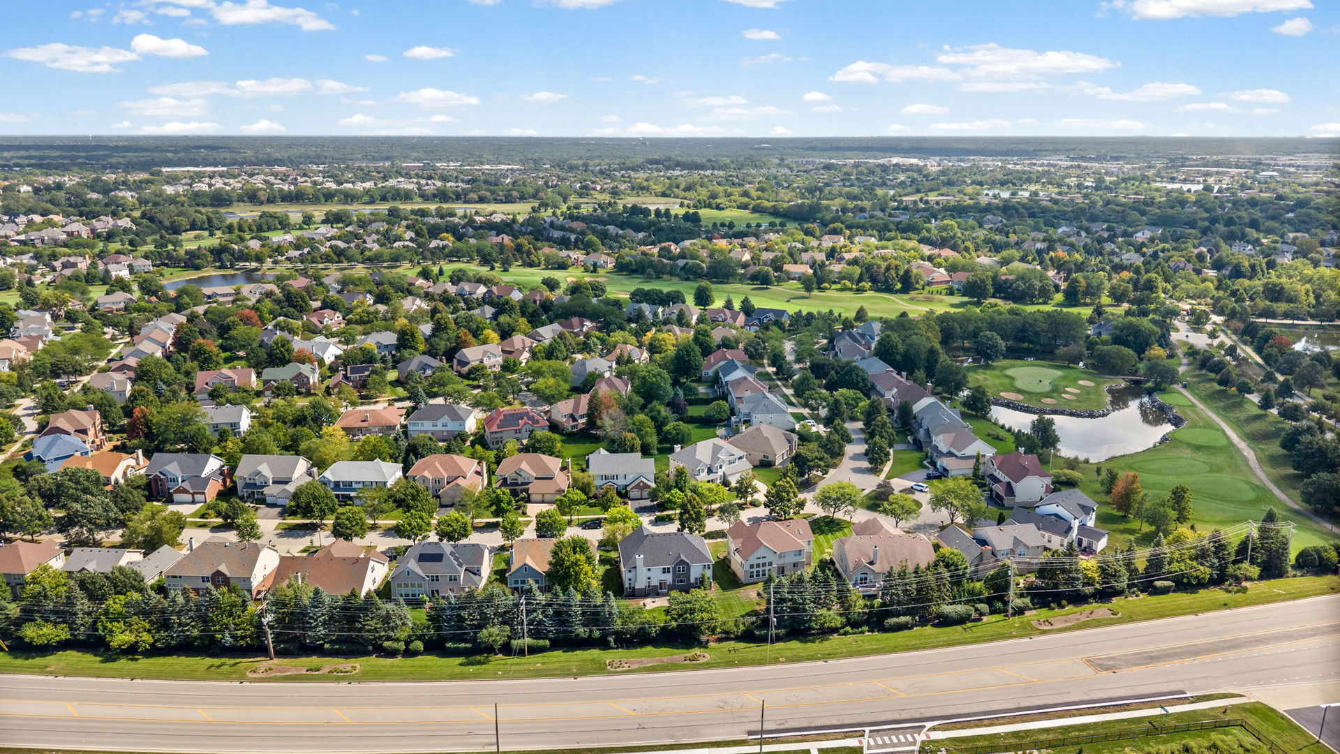 Aerial view of a residential neighborhood beside a golf course and pond.