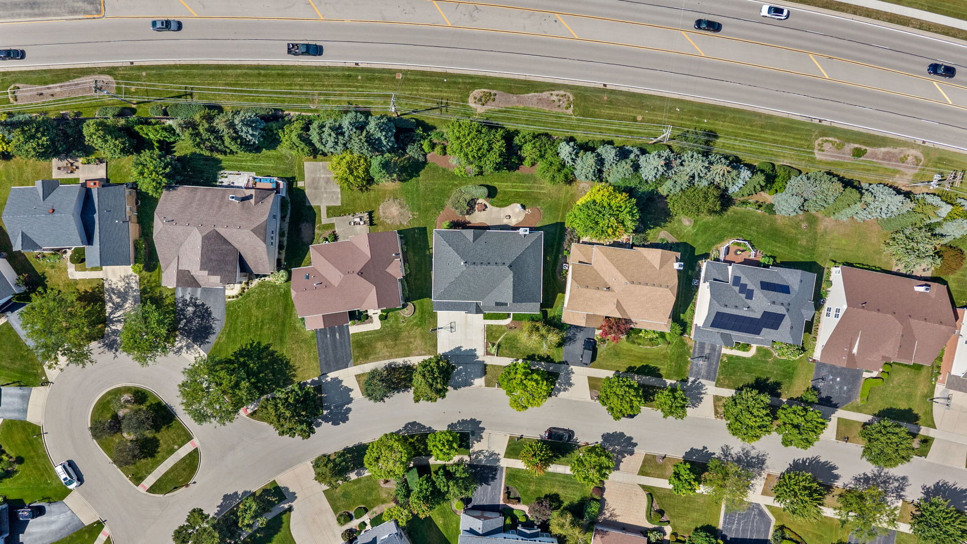 Aerial view of detached homes and landscaped yards beside a divided road.