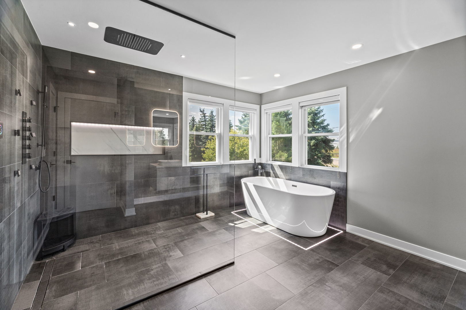 Modern bathroom with glass-enclosed shower, freestanding tub, and large windows.