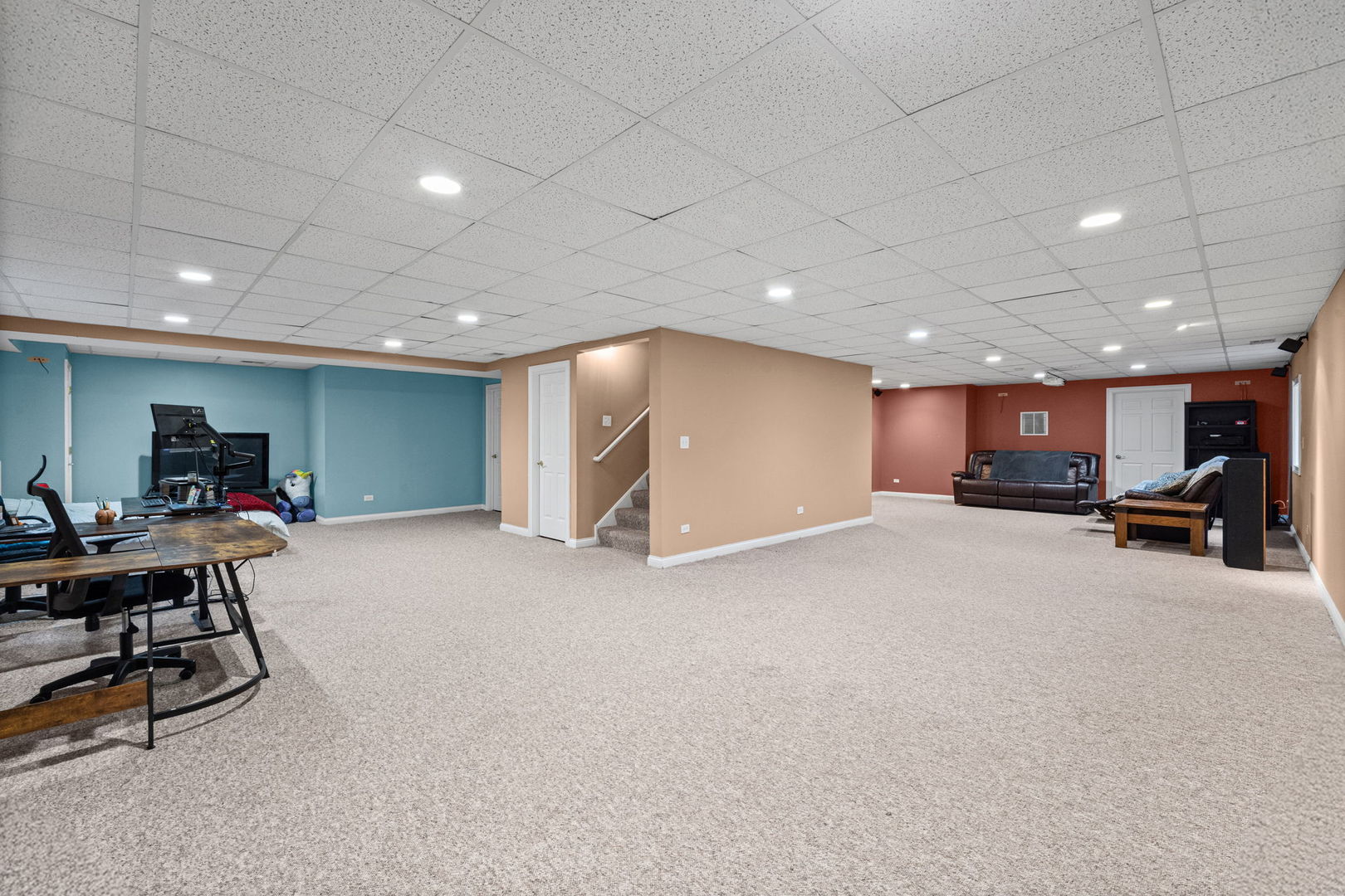 Basement recreation room with carpet, a central stairway, a computer workstation, and a sofa seating area.
