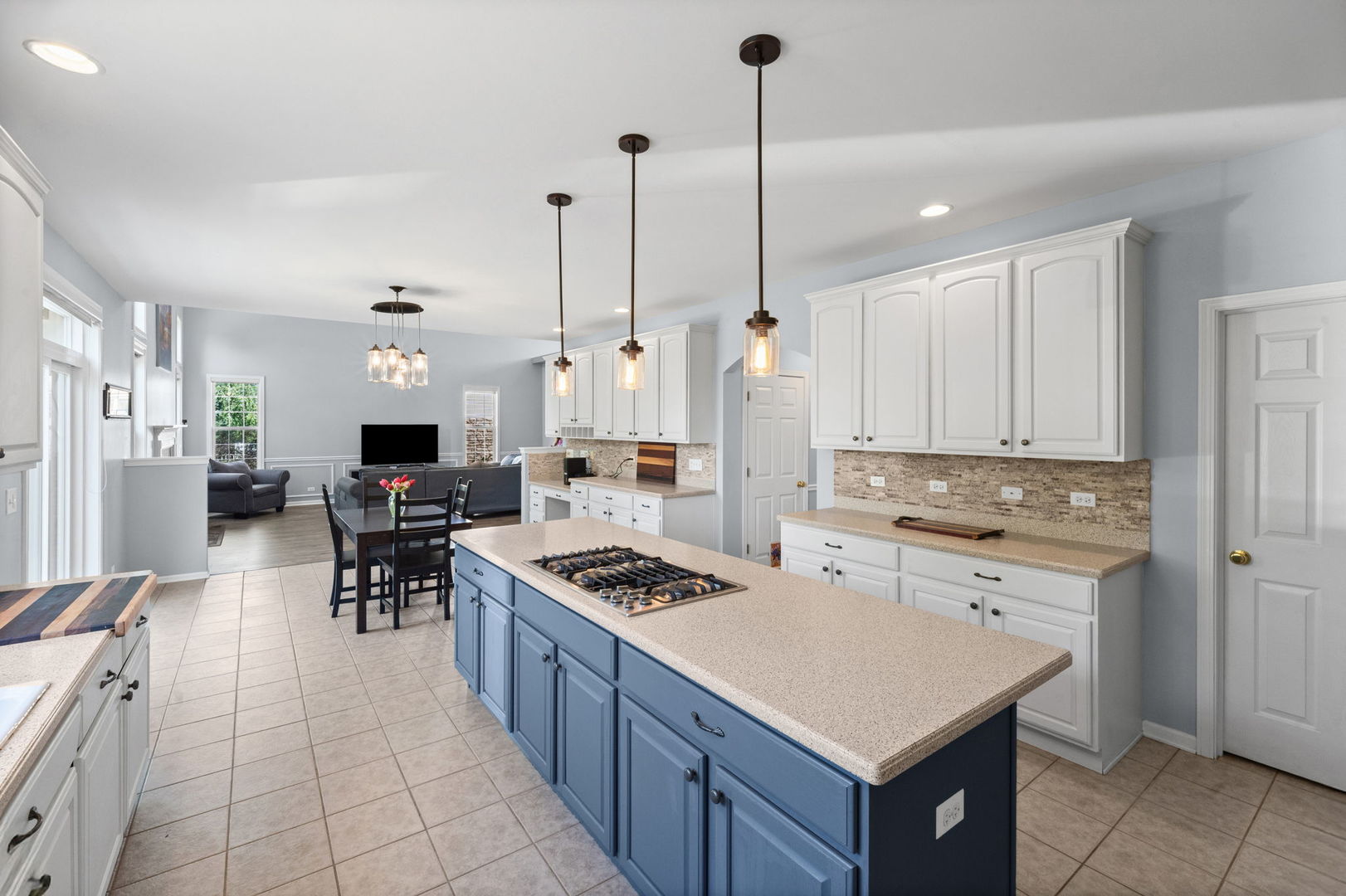 Open-plan kitchen with a large blue island, gas cooktop, white cabinets, and adjoining living area.