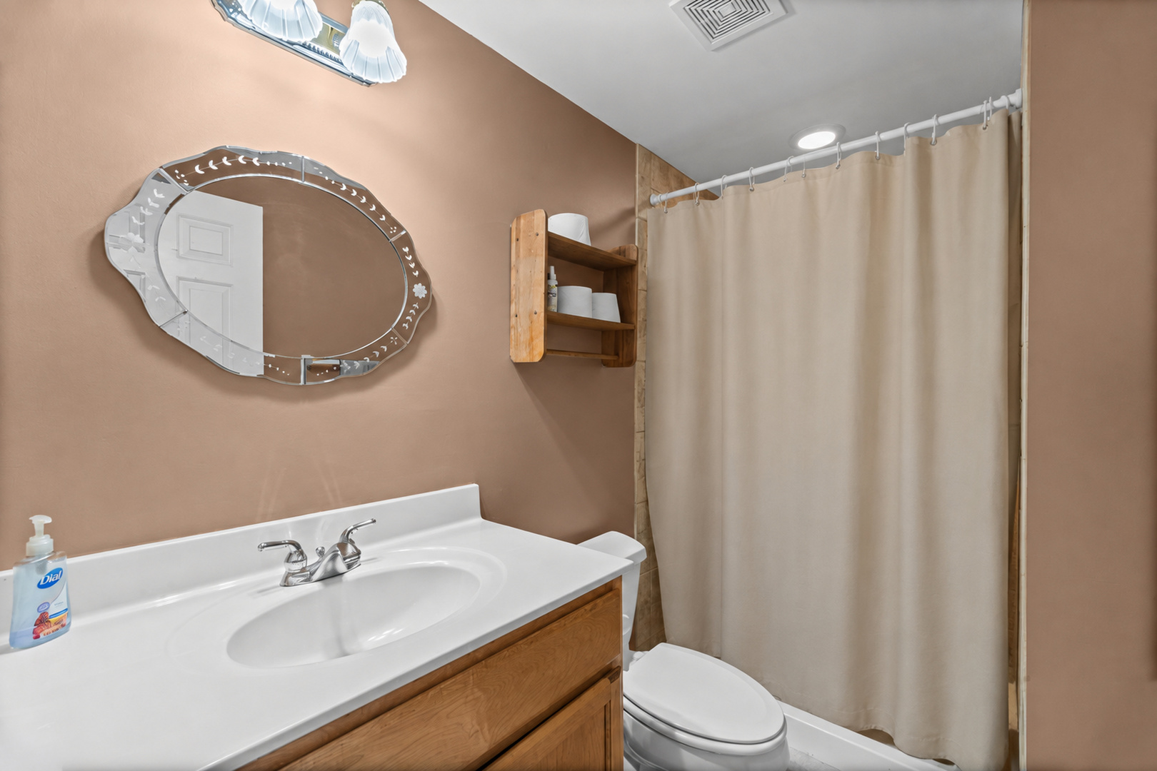 Bathroom with wood vanity, white sink, oval mirror, toilet, and curtained tub-shower.