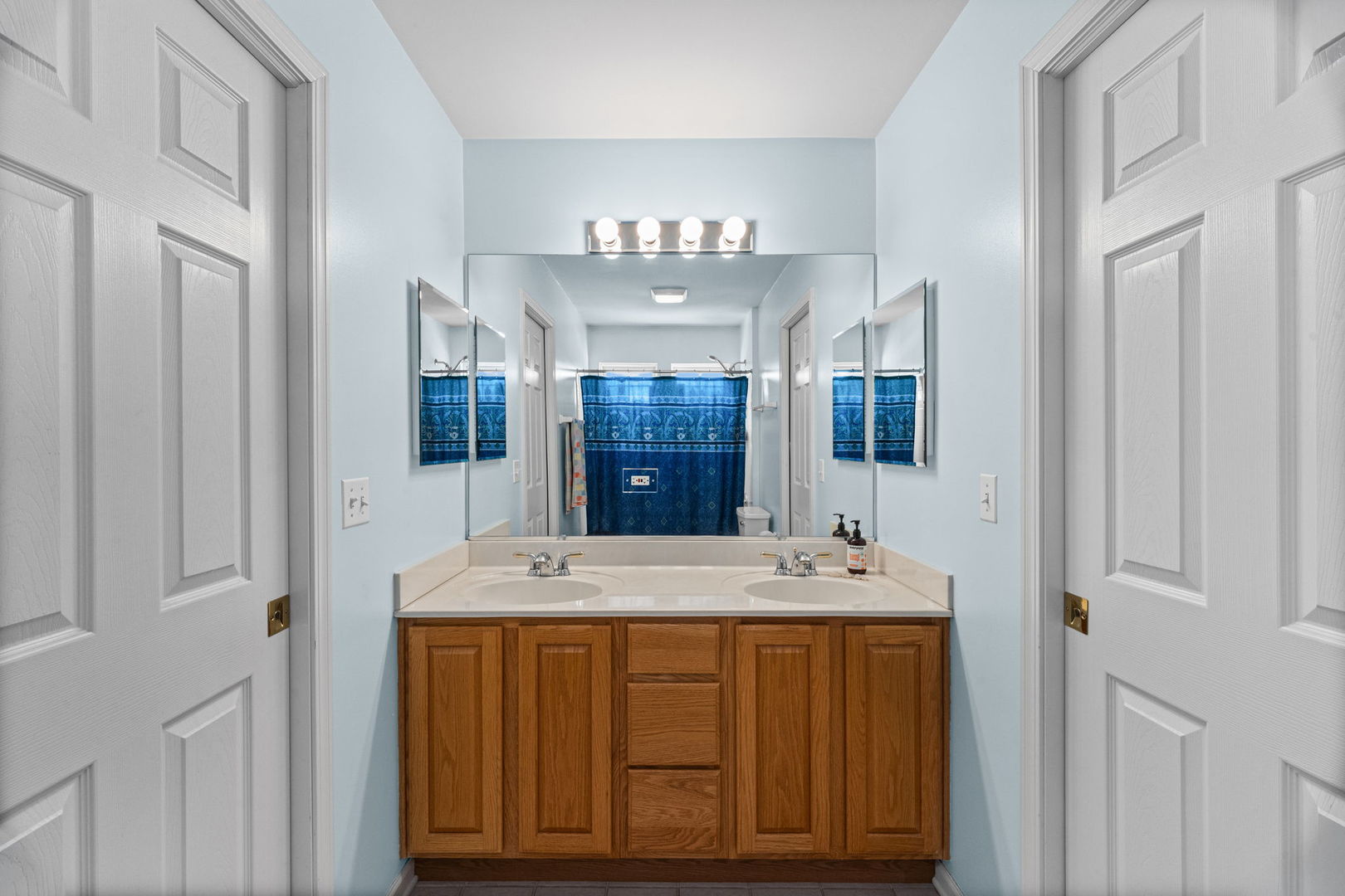 Bathroom with a double-sink wood vanity, wide mirror, and blue shower curtain.