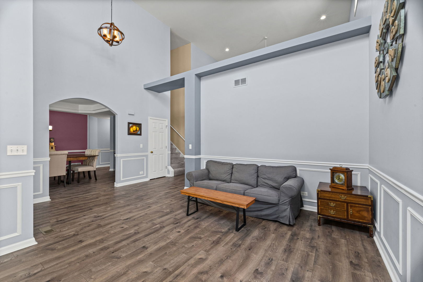 Living room with a gray sofa, high ceilings, wood-look floors, and an arched opening to the dining area.