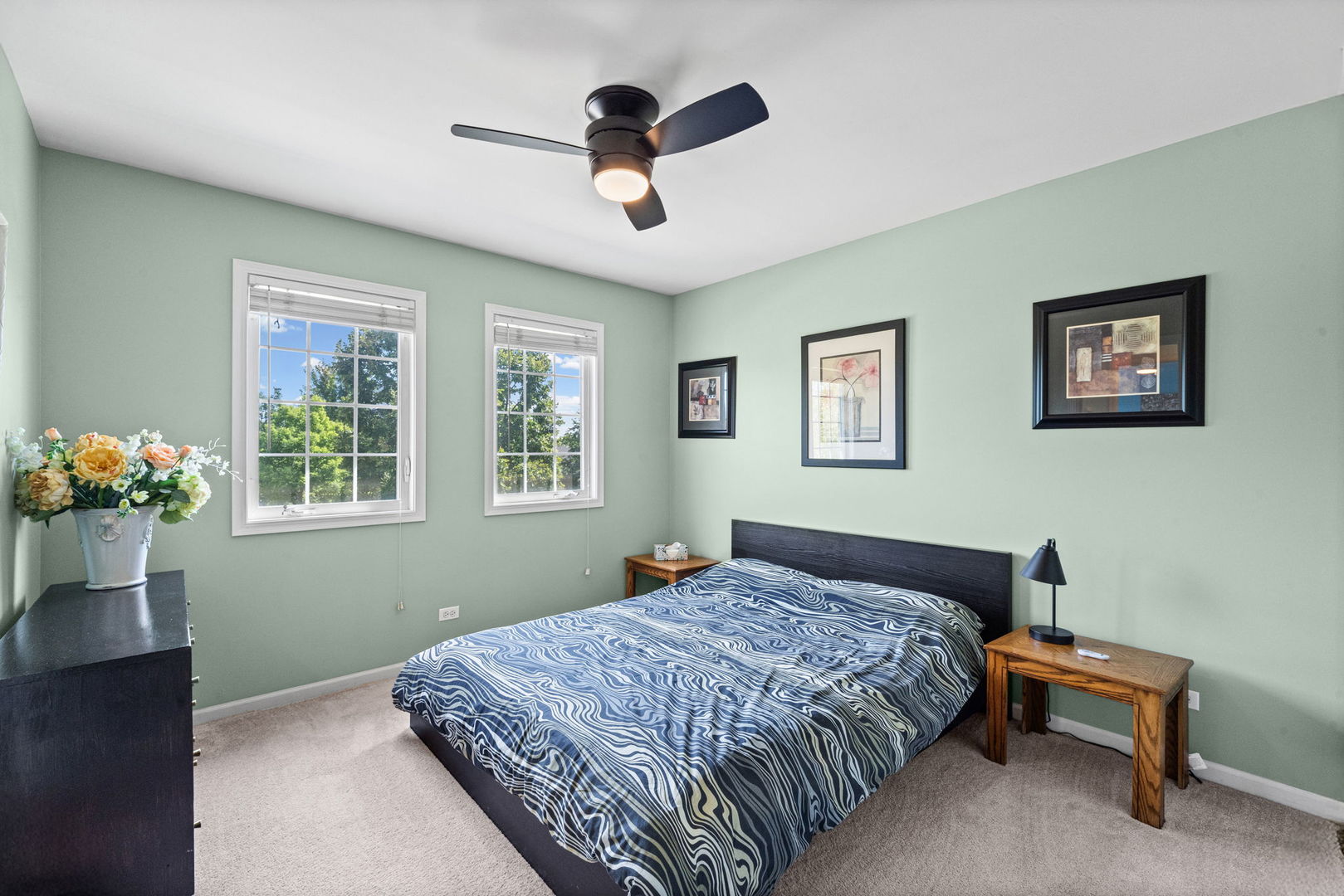 Bedroom with pale green walls, patterned blue bedding, two windows, and a ceiling fan.