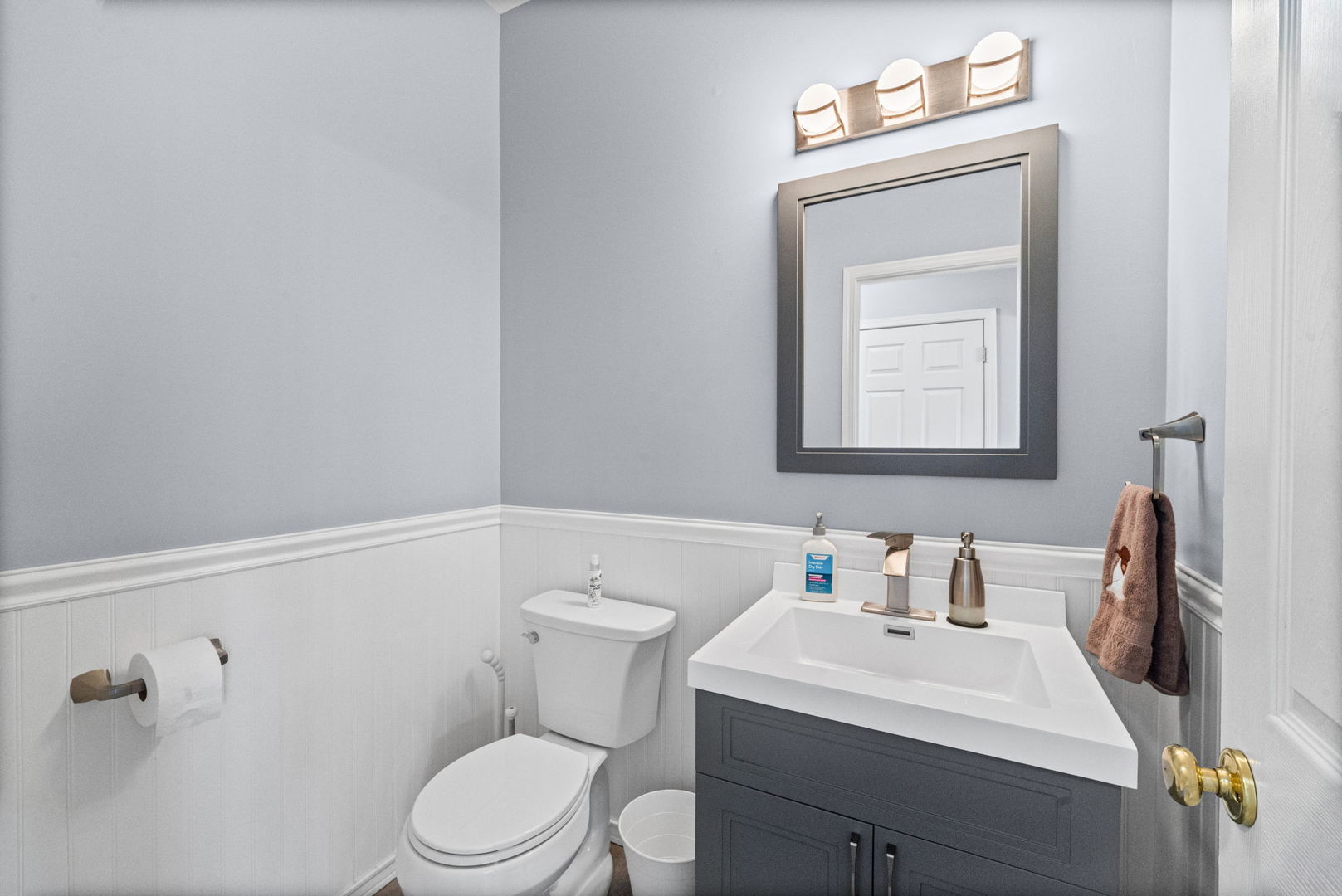 Bathroom with a dark gray vanity, white sink and toilet, and a large framed mirror.