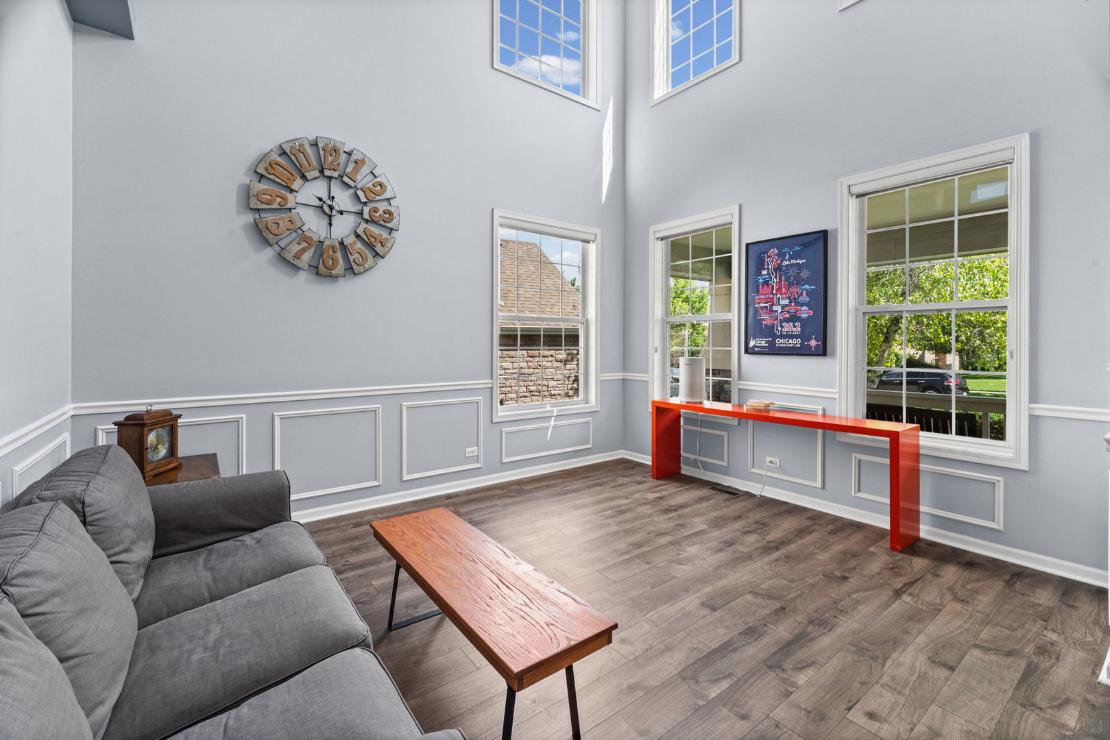Bright living room with a vaulted ceiling, tall windows, gray sectional, and red console table.