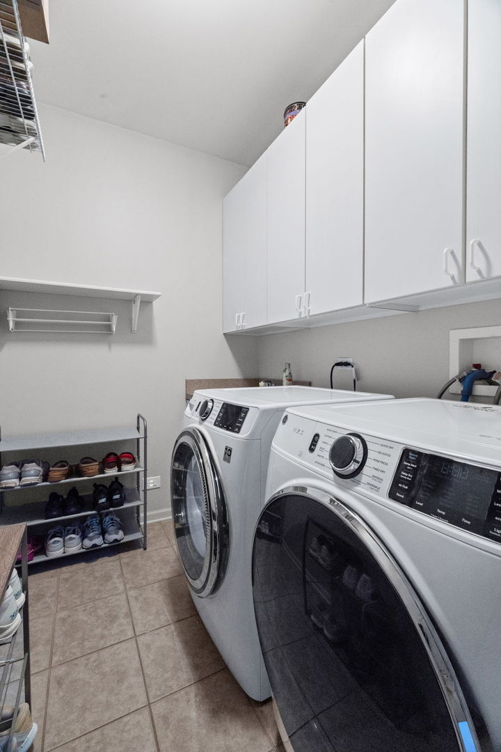 Laundry room with front-loading washer and dryer beneath white cabinets, with a shoe rack along the wall.