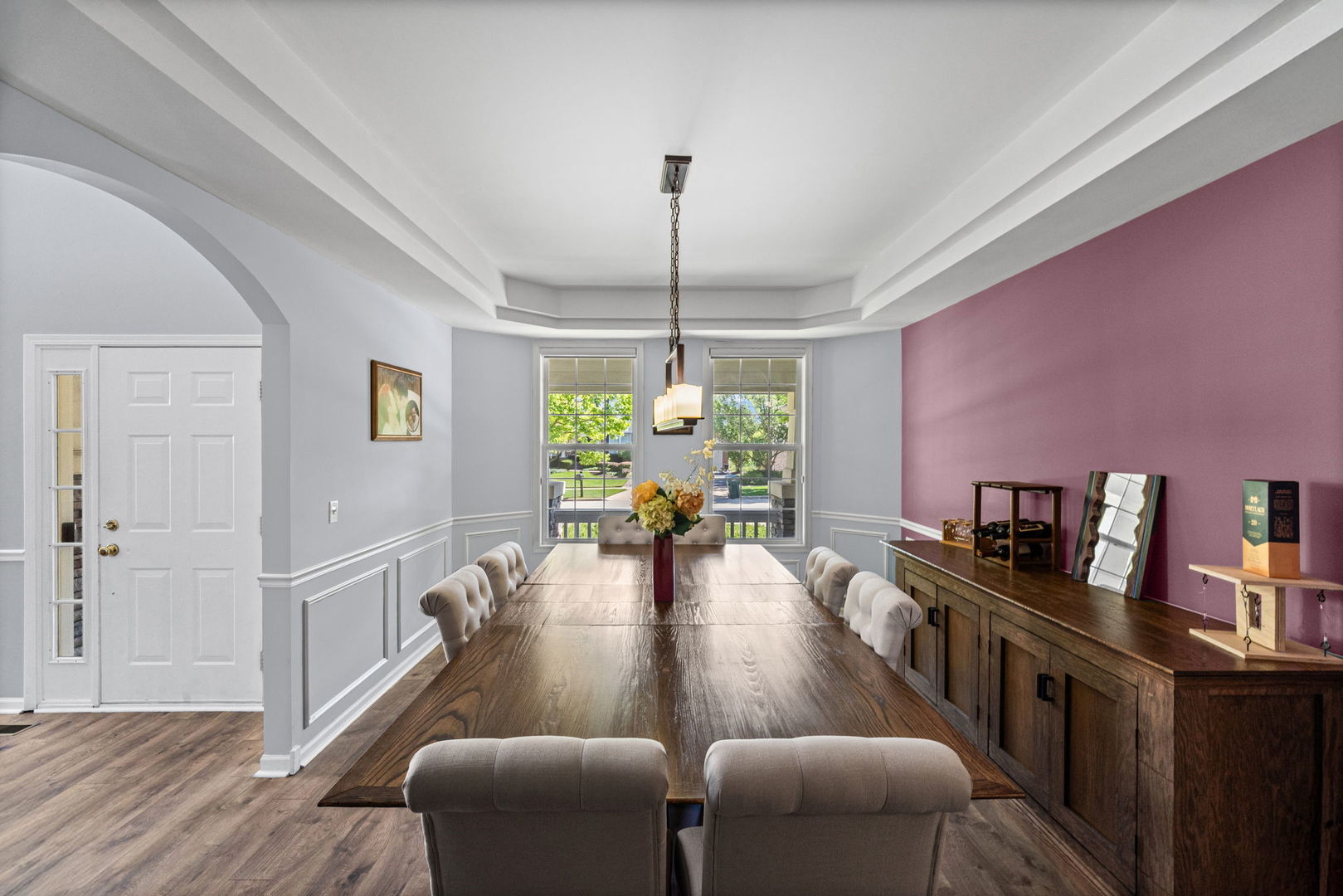 Dining room with a long wooden table, tray ceiling, and mauve accent wall.