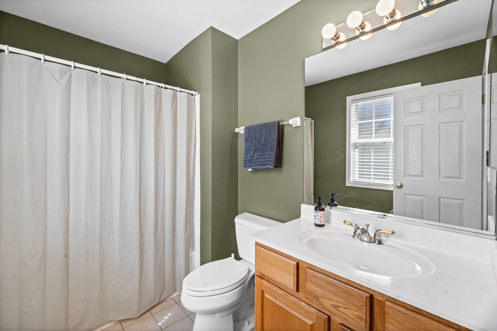 Bathroom with an olive-green wall, white shower curtain, and wood vanity.