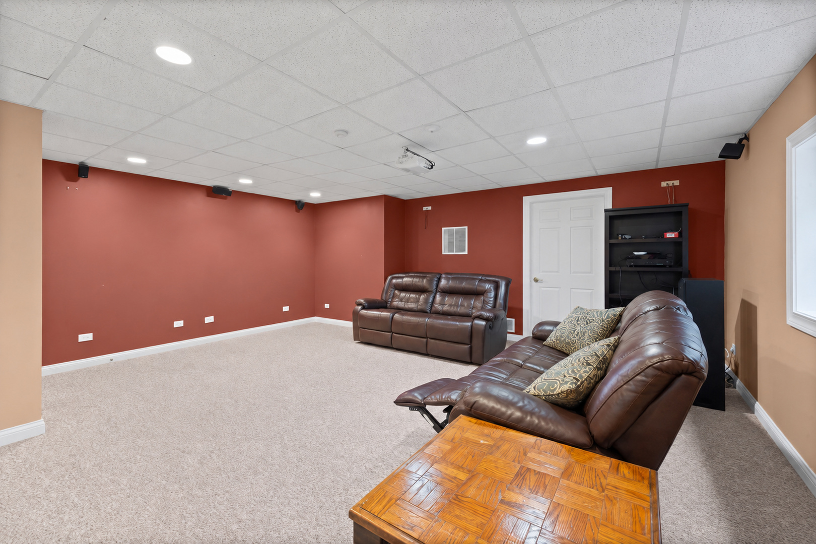 Furnished recreation room with leather reclining sofas, red walls, and a ceiling-mounted projector.