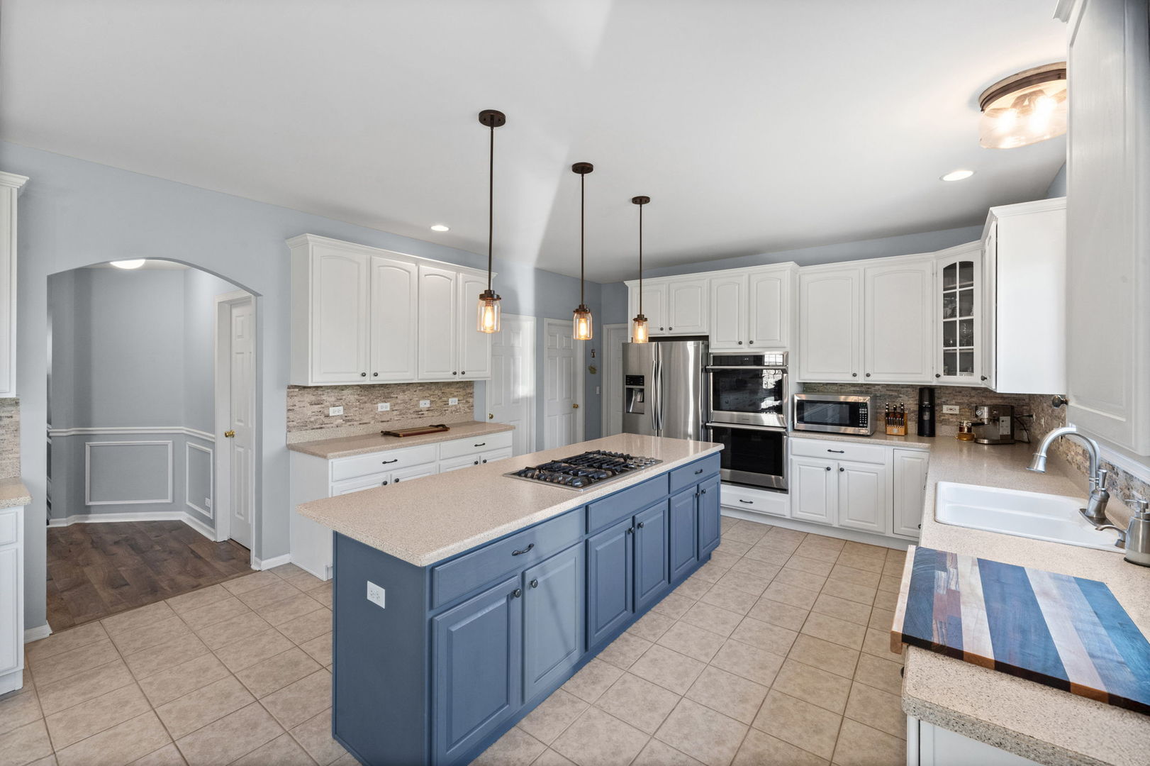 Kitchen with white cabinets, blue island and gas cooktop, stainless appliances, and a farmhouse sink.