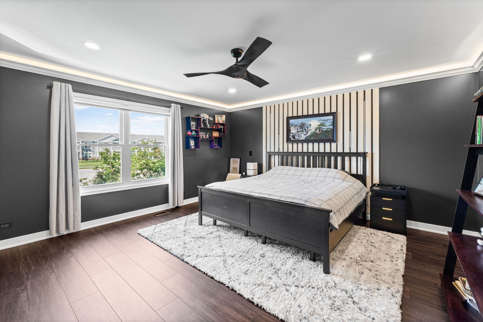 Bedroom with a striped accent wall behind the bed, white shag rug, and large window.