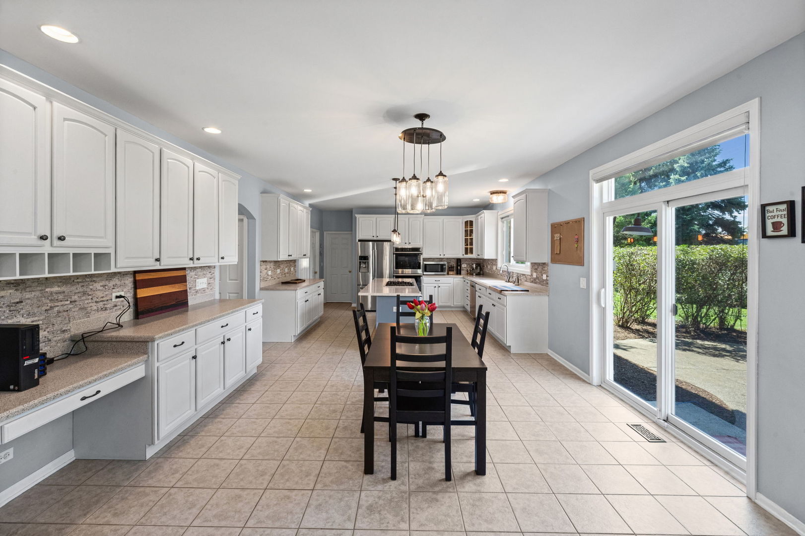 Bright kitchen with white cabinets, stainless steel appliances, and a dining table beside sliding glass doors.