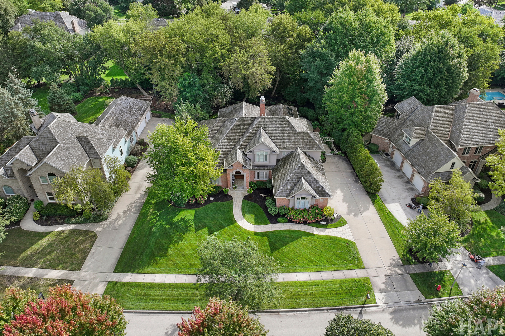 Aerial view of a landscaped brick home with a curved front walk and mature trees.