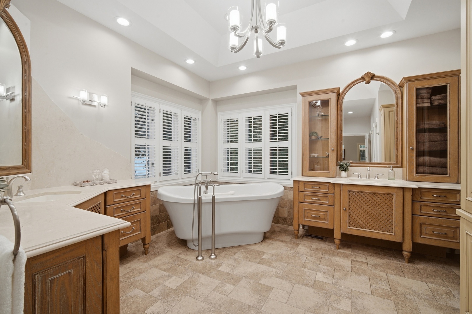 Spacious bathroom with a freestanding tub, shuttered windows, and warm wood cabinetry.