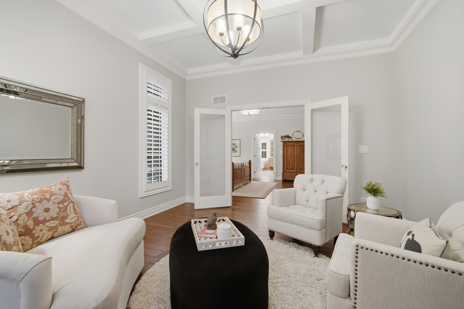 Living room with white seating, a black ottoman, and open doors to an adjoining room.