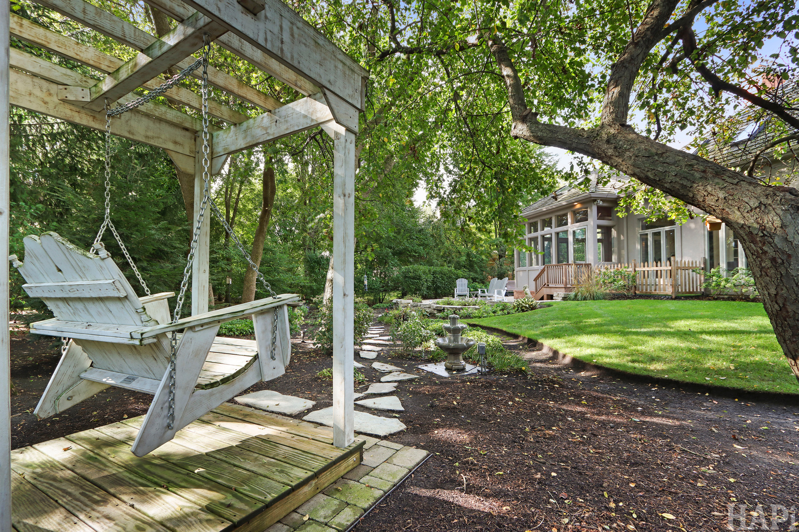 Backyard with a pergola swing, stone path, fountain, and glass-enclosed sunroom.