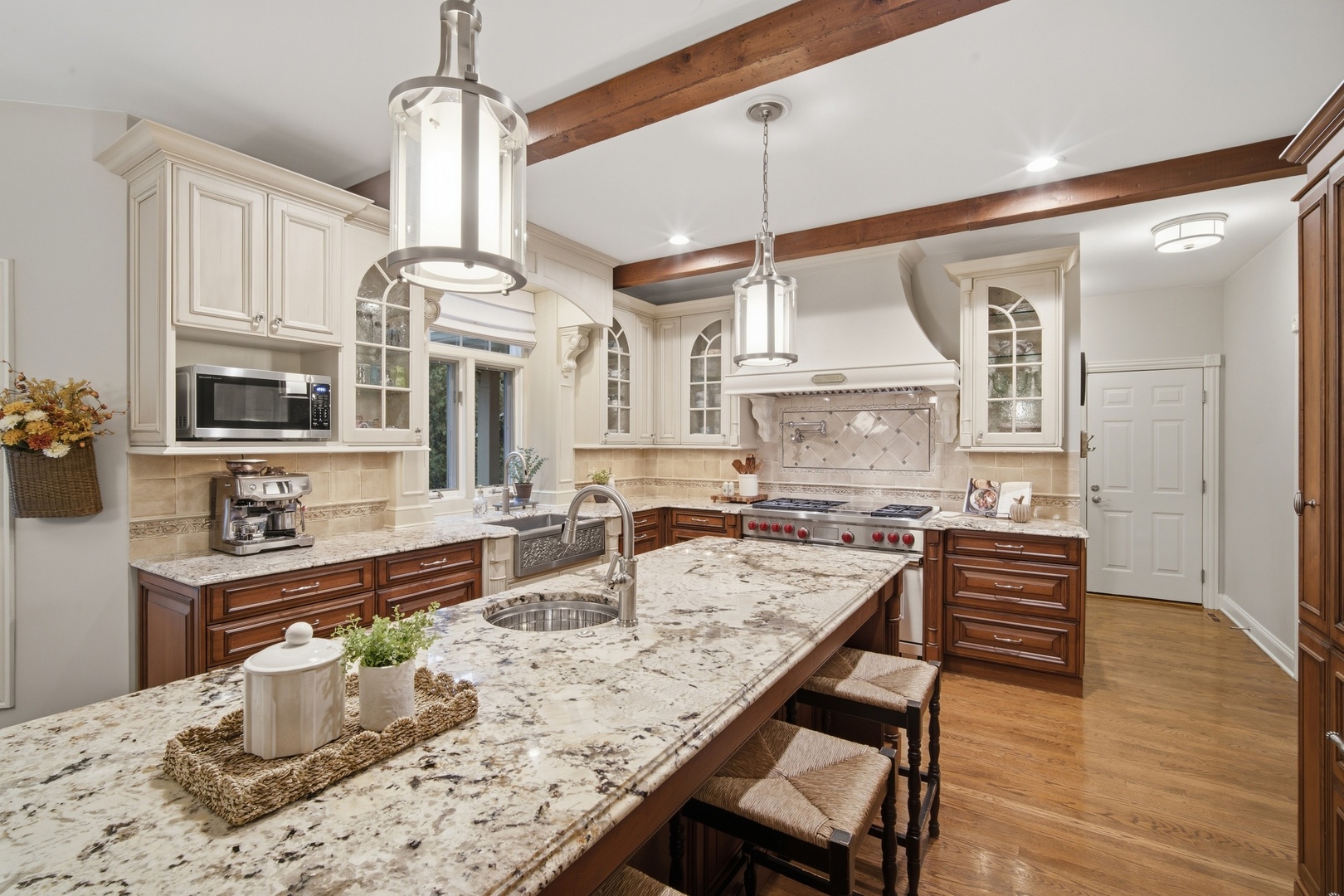 Kitchen with a large granite island, cream cabinetry, exposed wood beams, and a stainless steel range.