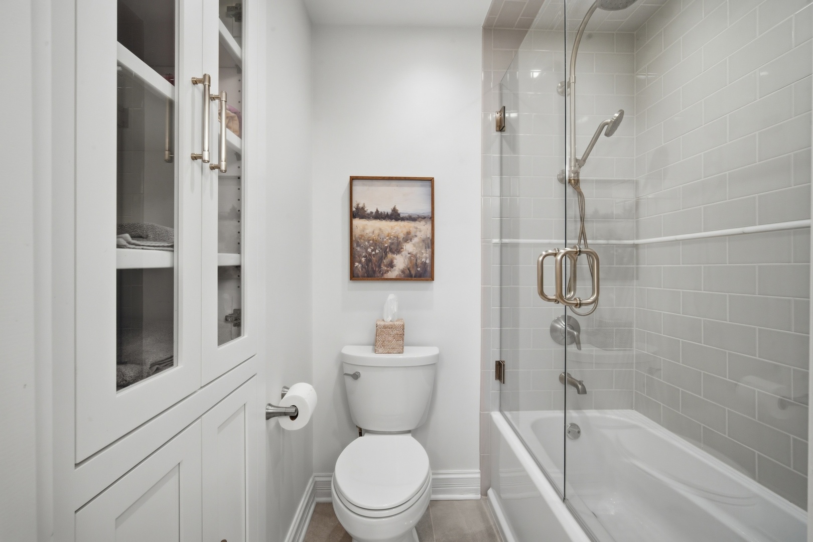 Bathroom with built-in linen cabinets and a glass-enclosed tub and shower with gray subway tile.
