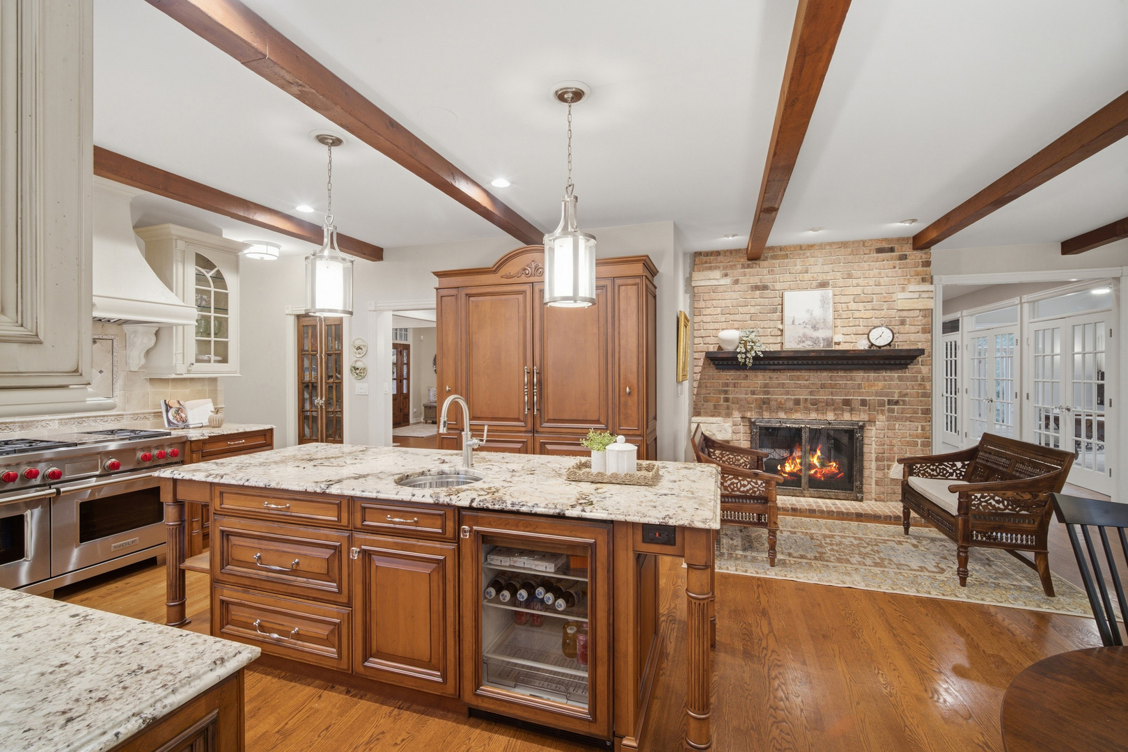 Kitchen with a granite island, rich wood cabinetry, exposed beams, and an adjoining brick fireplace.