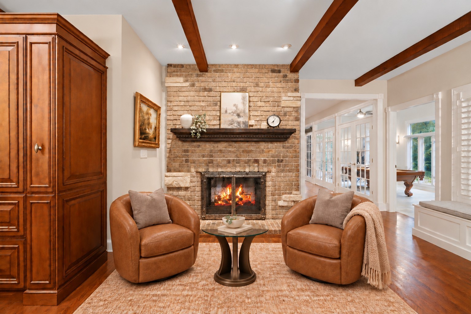 Living room with a brick fireplace, exposed wood beams, and two tan leather armchairs.