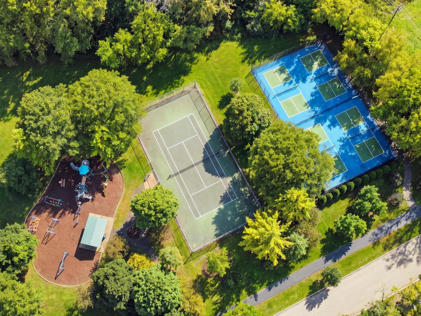 Aerial view of tennis courts and a playground surrounded by mature trees.