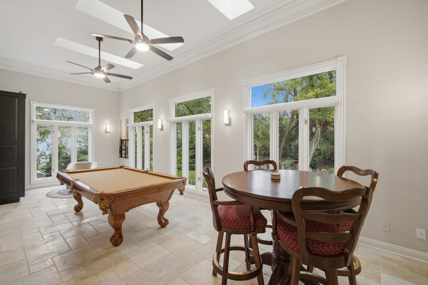 Game room with a billiard table, round dining table, and large windows overlooking trees.