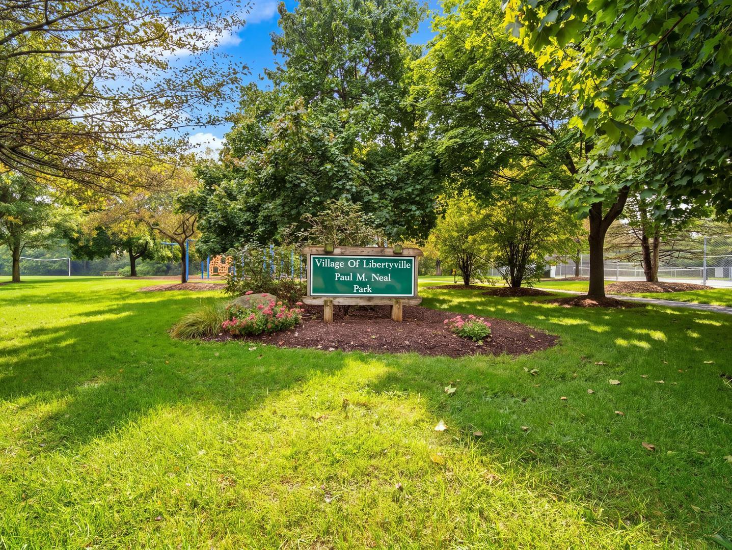 Village of Libertyville Paul M. Neal Park sign in a landscaped lawn beneath mature trees.