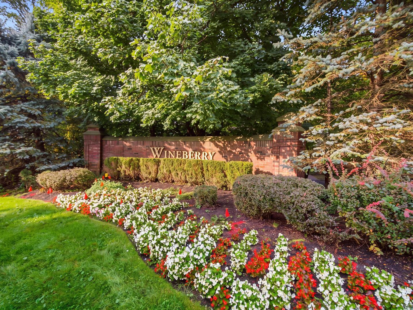 Wineberry neighborhood entrance sign framed by mature trees and colorful flower beds.